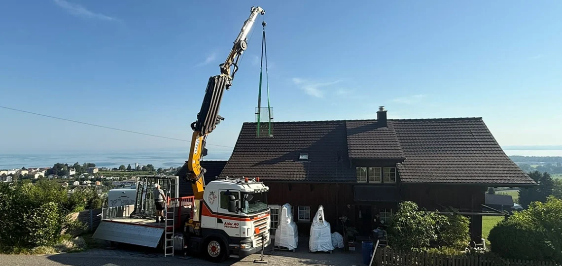 Kran hebt Holz-Aluminium-Fenster über Einfamilienhaus zur Montage.