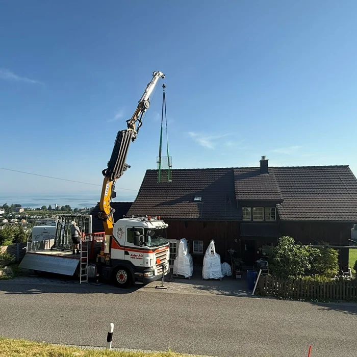 Kran hebt Holz-Aluminium-Fenster über Einfamilienhaus zur Montage.